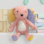 Pink plush toy with colorful accents on a white surface with wooden letters and pastel books in the background.