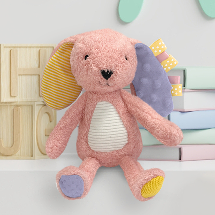 Pink plush toy with colorful accents on a white surface with wooden letters and pastel books in the background.