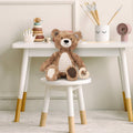 Teddy bear on a small white stool with a white table in the background
