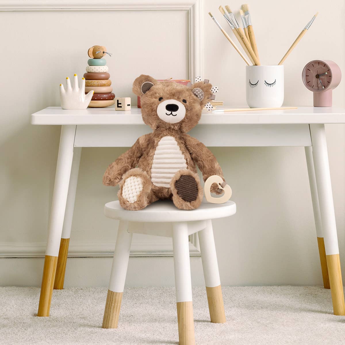 Teddy bear on a small white stool with a white table in the background
