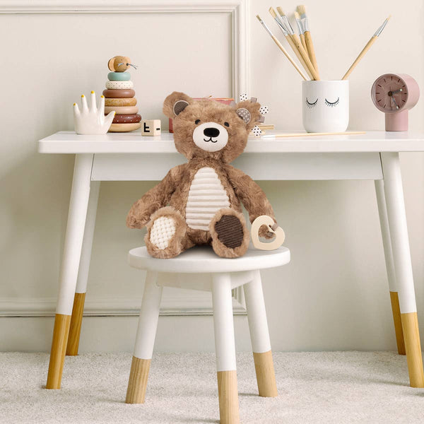 Teddy bear on a small white stool with a white table in the background