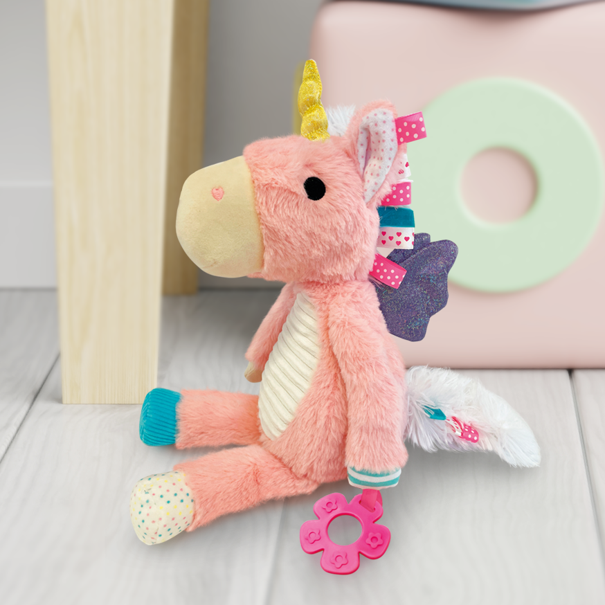 Pink plush unicorn toy with a teether on a wooden floor