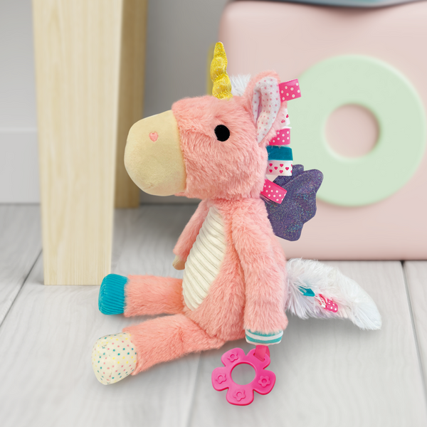 Pink plush unicorn toy with a teether on a wooden floor