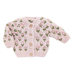 A light pink hand-knit baby cardigan sweater with a floral pattern in pink and green, featuring three wooden buttons down the front, laid flat on a white background. AdoraBaby.co.uk