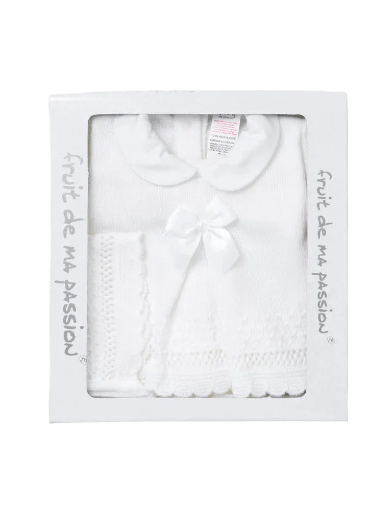 A white baby outfit set in its original white packaging box, featuring a short-sleeve knit top with a Peter Pan collar and a matching knitted bow, alongside a knitted bootie.