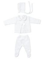 A three-piece white baby outfit set including a long-sleeve knit romper with a Peter Pan collar and bow, matching footed pants, and a bonnet with ties, laid out on a light gray background.