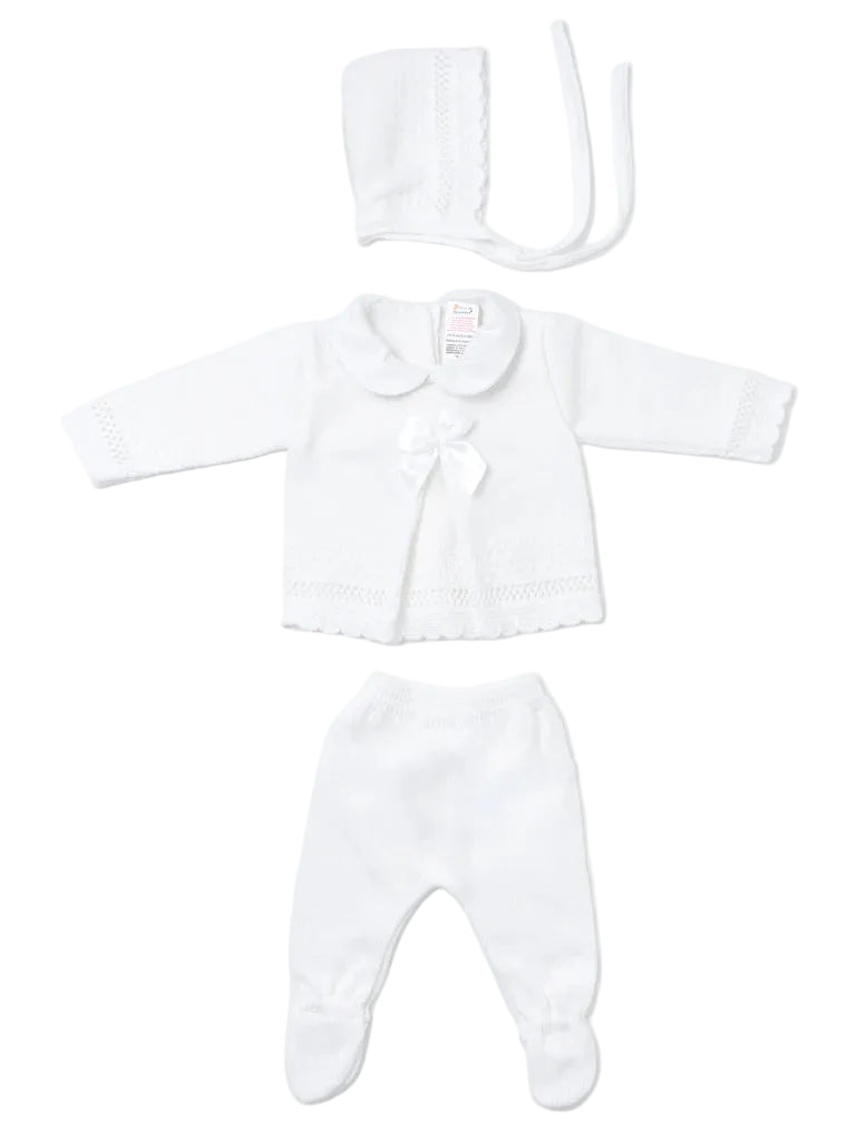 A three-piece white baby outfit set including a long-sleeve knit romper with a Peter Pan collar and bow, matching footed pants, and a bonnet with ties, laid out on a light gray background.