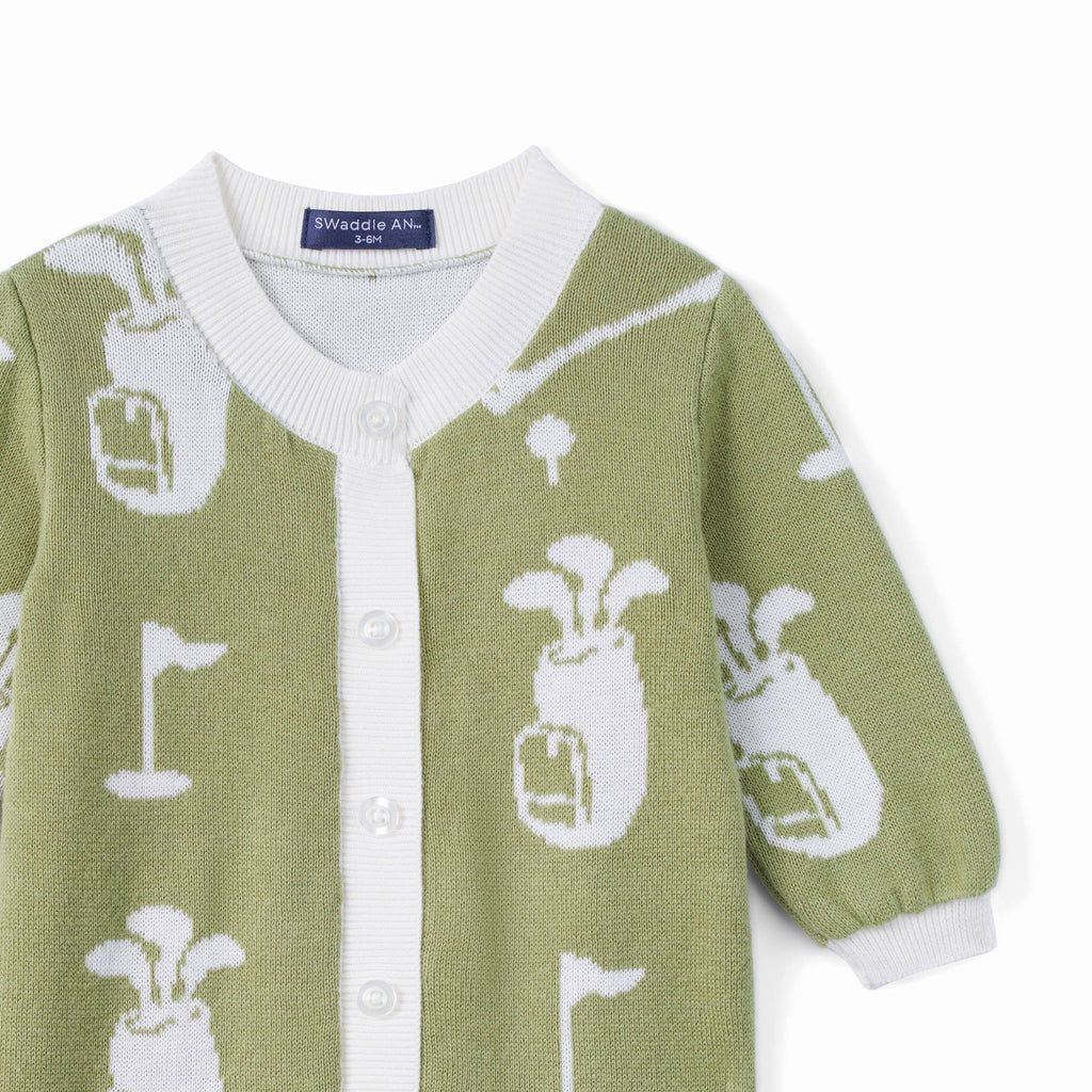 A close-up of a knitted cardigan sweater in sage green with a white golf-themed pattern, featuring a white ribbed collar, button-front placket, and white cuffs.