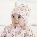 Baby wearing a pink knitted outfit with floral patterns on a white background