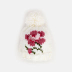 A white knit beanie with a fluffy white pom-pom and a knitted floral pattern in pink and green on the front, shown against a plain white background. AdoraBaby.co.uk