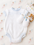 Adorababy.co.uk baby knit romper set in white with light blue trim, shown with matching white booties and a small teddy bear toy on a patterned white background. A gift box is partially visible at the top right.