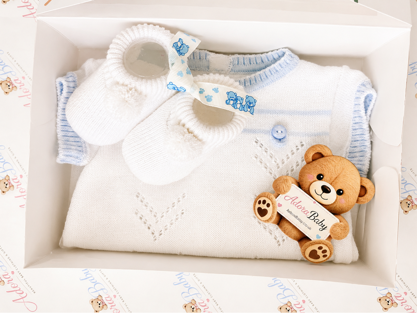 AdoraBaby.co.uk baby gift set in a white box featuring a white knit baby sweater with light blue trim, a pair of white bootie socks with a blue bow, 