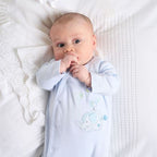 Baby wearing a light blue onesie with a cartoon design, lying on a white textured surface.