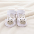 A close-up of a baby's feet wearing white baby socks with a giraffe design, resting on a soft beige fleece blanket. Adorababy.co.uk
