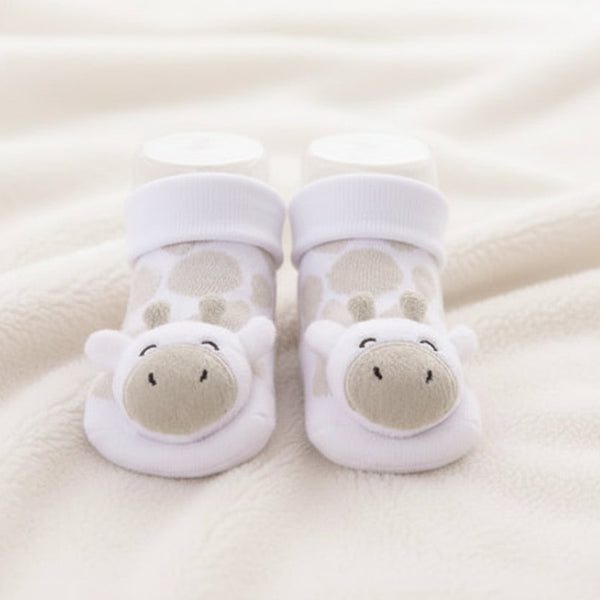 A close-up of a baby's feet wearing white baby socks with a giraffe design, resting on a soft beige fleece blanket. Adorababy.co.uk