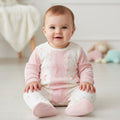 Baby wearing a pink and white outfit sitting on a light-colored floor.