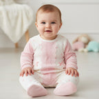 Baby wearing a pink and white outfit sitting on a light-colored floor.