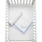 White crib with a blue and white blanket embroidered with 'Prince' on a white background