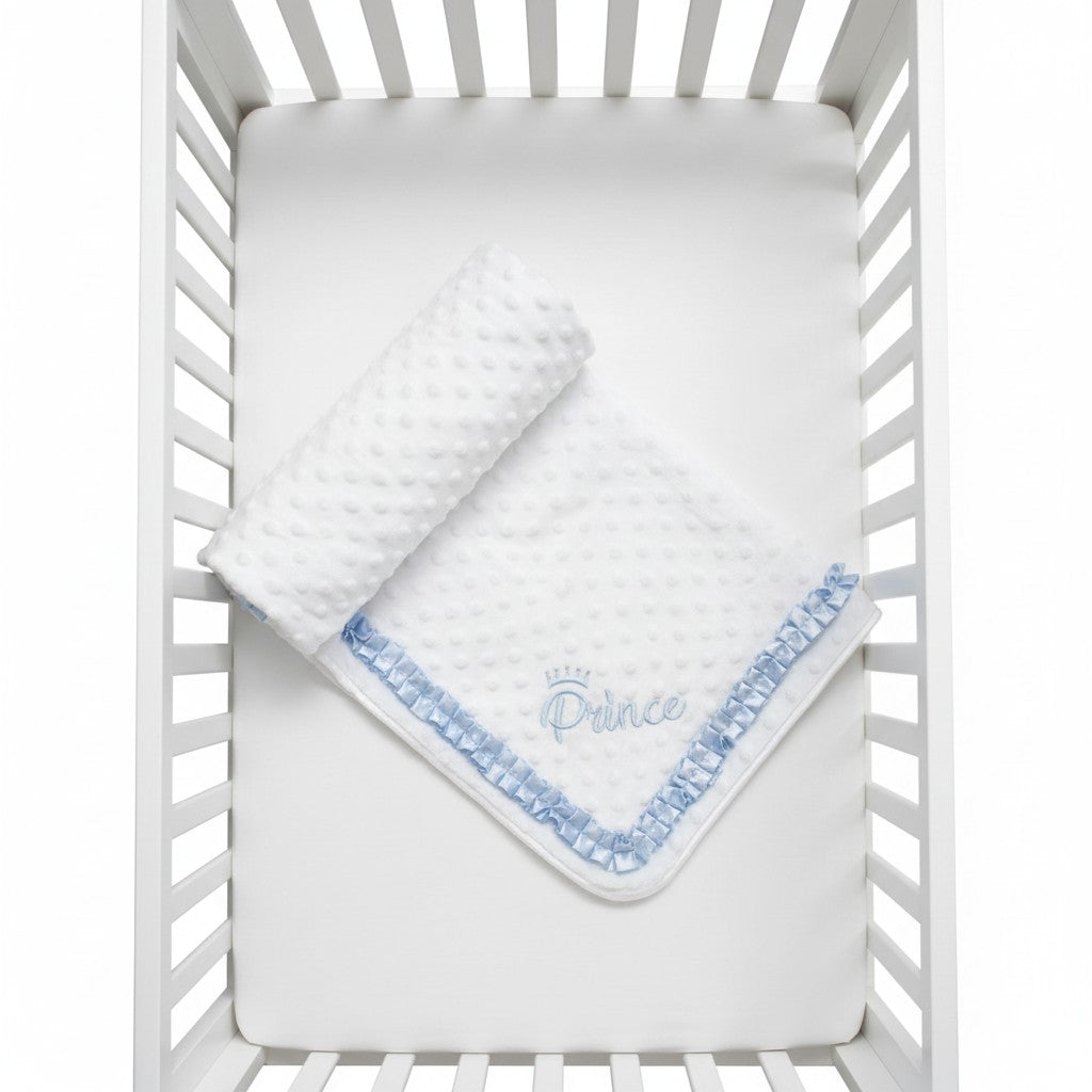 White crib with a blue and white blanket embroidered with 'Prince' on a white background
