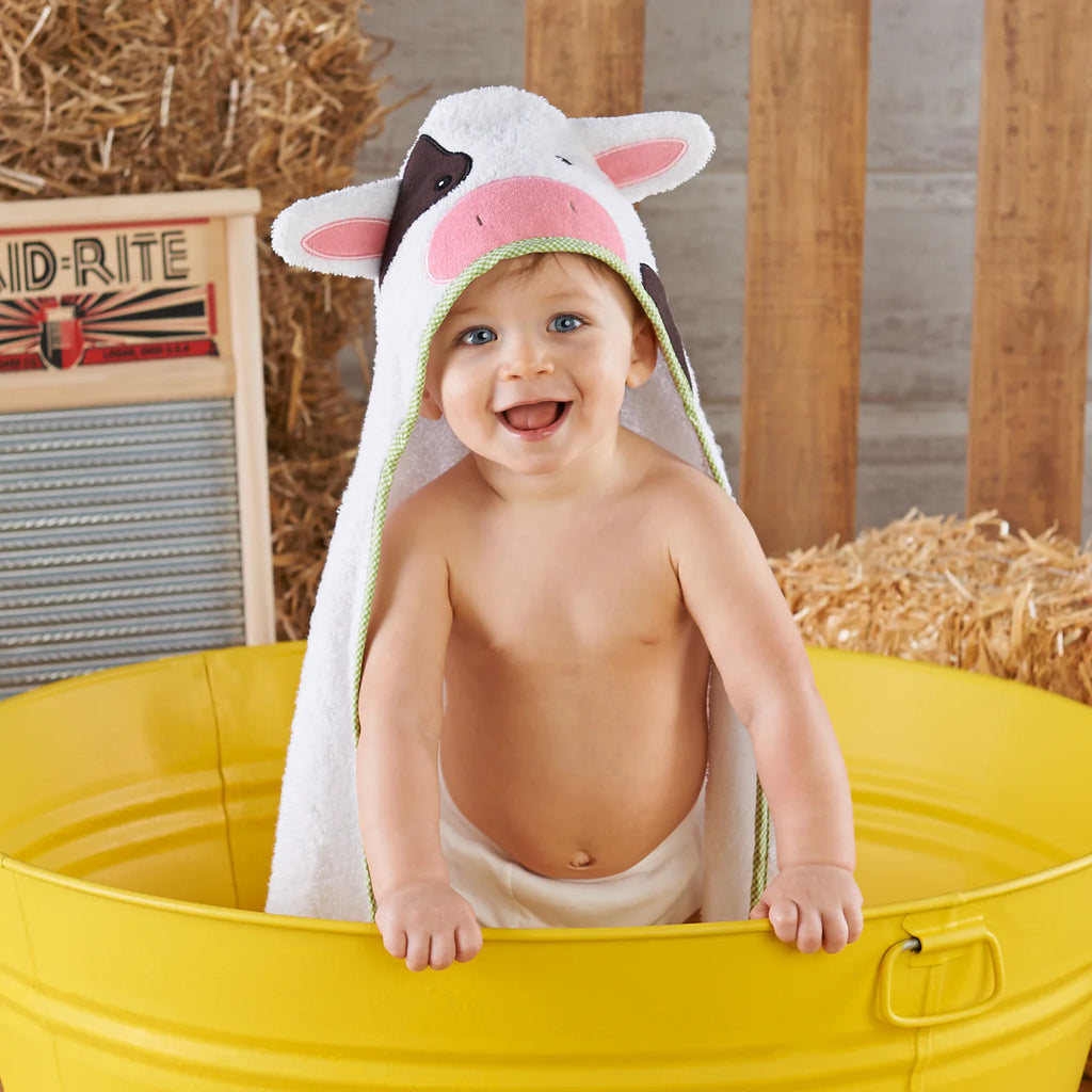 Child wearing a cow-themed hooded towel in a yellow tub with hay and a washboard in the background.