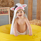 Child wearing a cow-themed hooded towel in a yellow tub with hay and a washboard in the background.