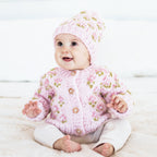 Baby wearing a pink knitted sweater and hat on a light background