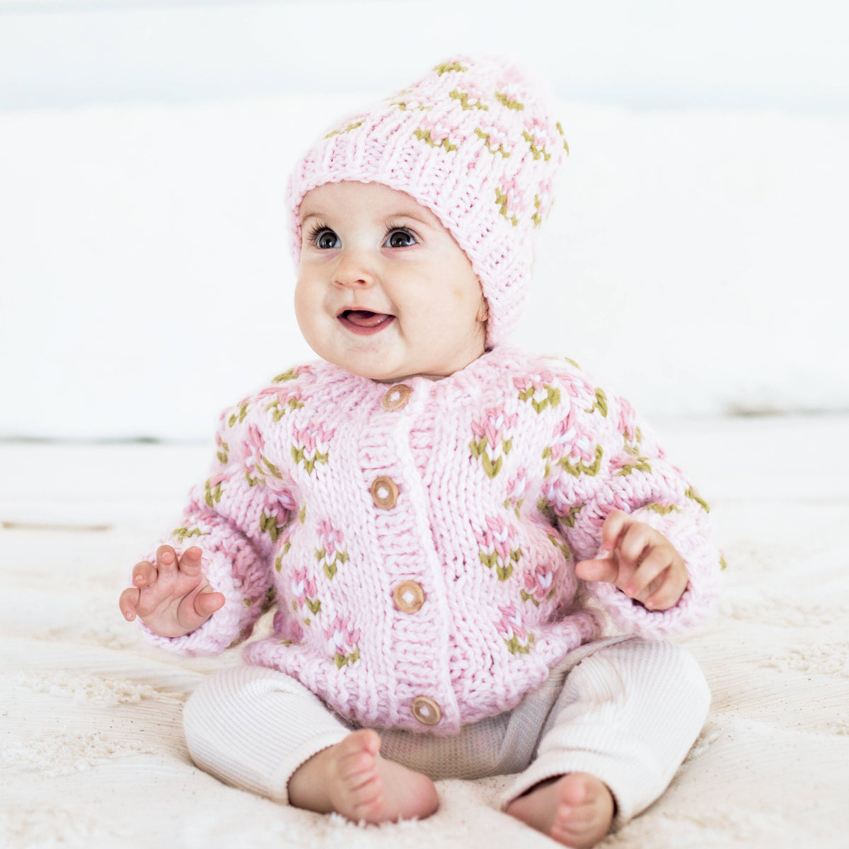 Baby wearing a pink knitted sweater and hat on a light background