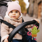Child in a stroller with a cactus toy, wearing a pink hat and beige coat.