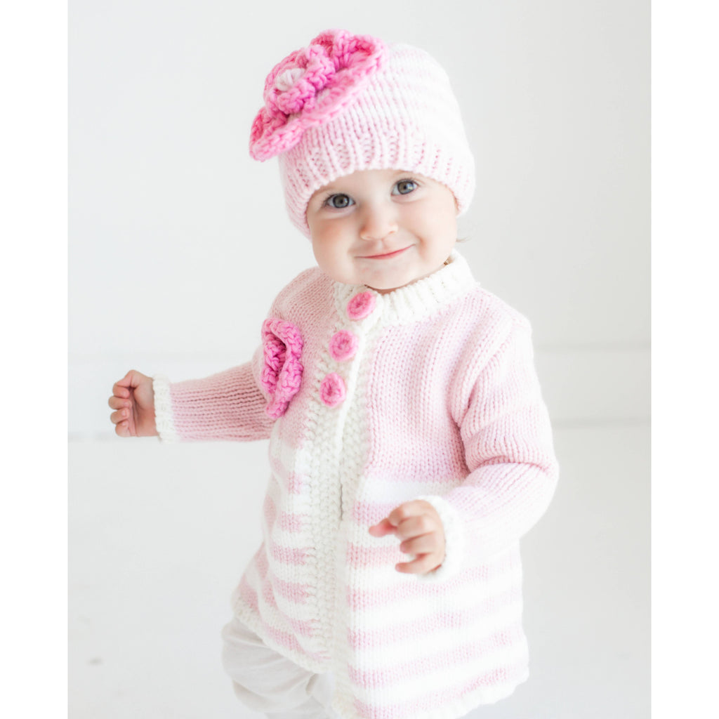 Baby wearing a pink knitted outfit with a matching hat on a white background