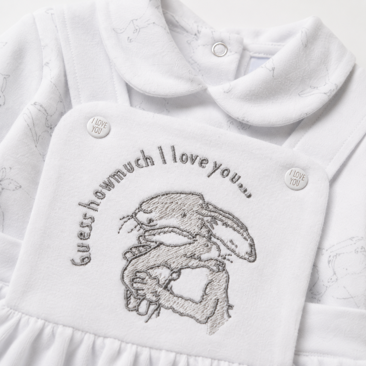 White baby outfit with embroidered design and text on a white background