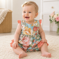 Baby wearing a floral dress sitting on a carpeted floor.