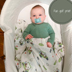 Baby in a crib with a green outfit and blue pacifier, surrounded by a golf-themed blanket.