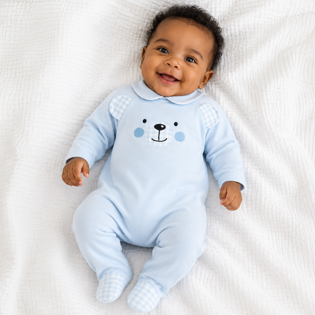 Baby wearing a light blue onesie with a bear face design on a white blanket