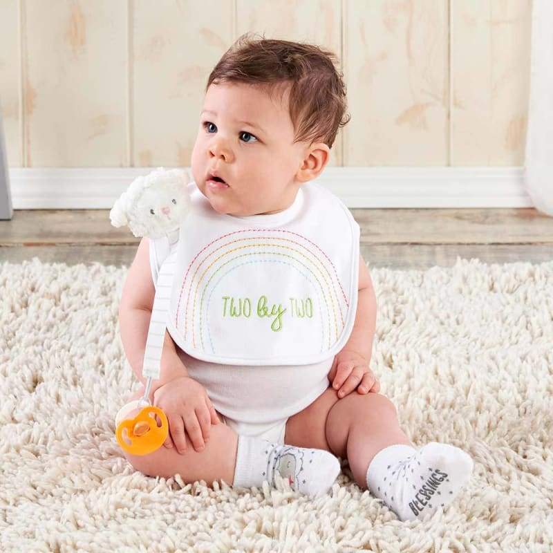 Baby sitting on a carpet wearing a bib with 'Two by Two' text
