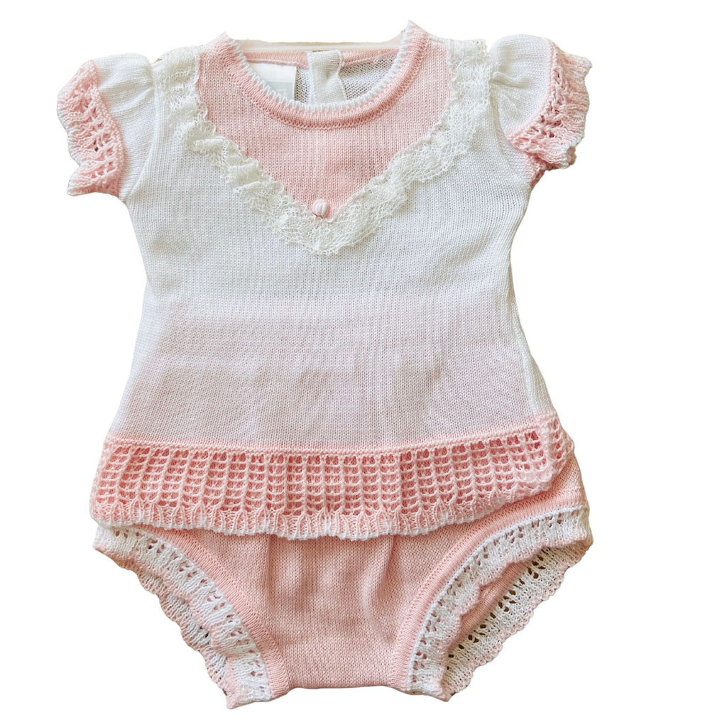 A baby knit romper in soft pink and white, featuring ruffled short sleeves, a lace-trimmed V-neckline, a textured crochet hem, and lace-trimmed leg openings.