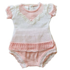 A baby knit romper in soft pink and white, featuring ruffled short sleeves, a lace-trimmed V-neckline, a textured crochet hem, and lace-trimmed leg openings.