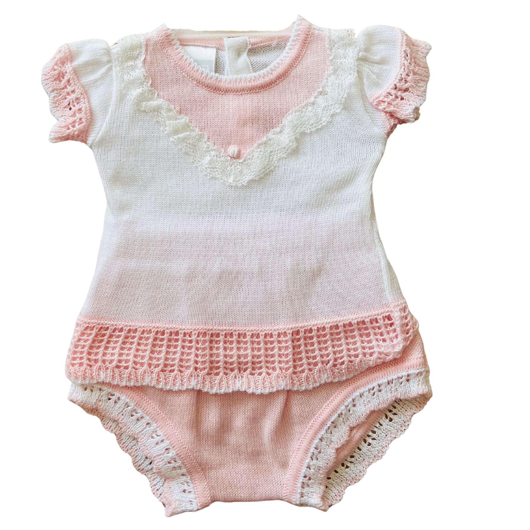 A baby knit romper in soft pink and white, featuring ruffled short sleeves, a lace-trimmed V-neckline, a textured crochet hem, and lace-trimmed leg openings.